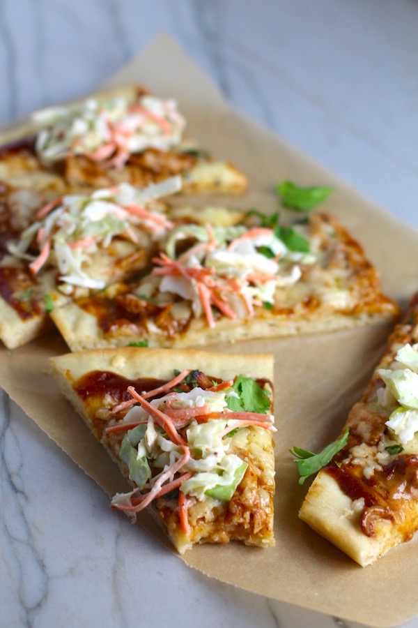 Sliced BBQ Chicken Pizza recipe with coleslaw and cilantro on top. It has homemade pizza crust, tangy and creamy BBQ sauce, hearty shredded chicken, cheddar cheese and coleslaw on top!   