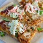 Sliced BBQ Chicken Pizza recipe with coleslaw and cilantro on top. It has homemade pizza crust, tangy and creamy BBQ sauce, hearty shredded chicken, cheddar cheese and coleslaw on top!   