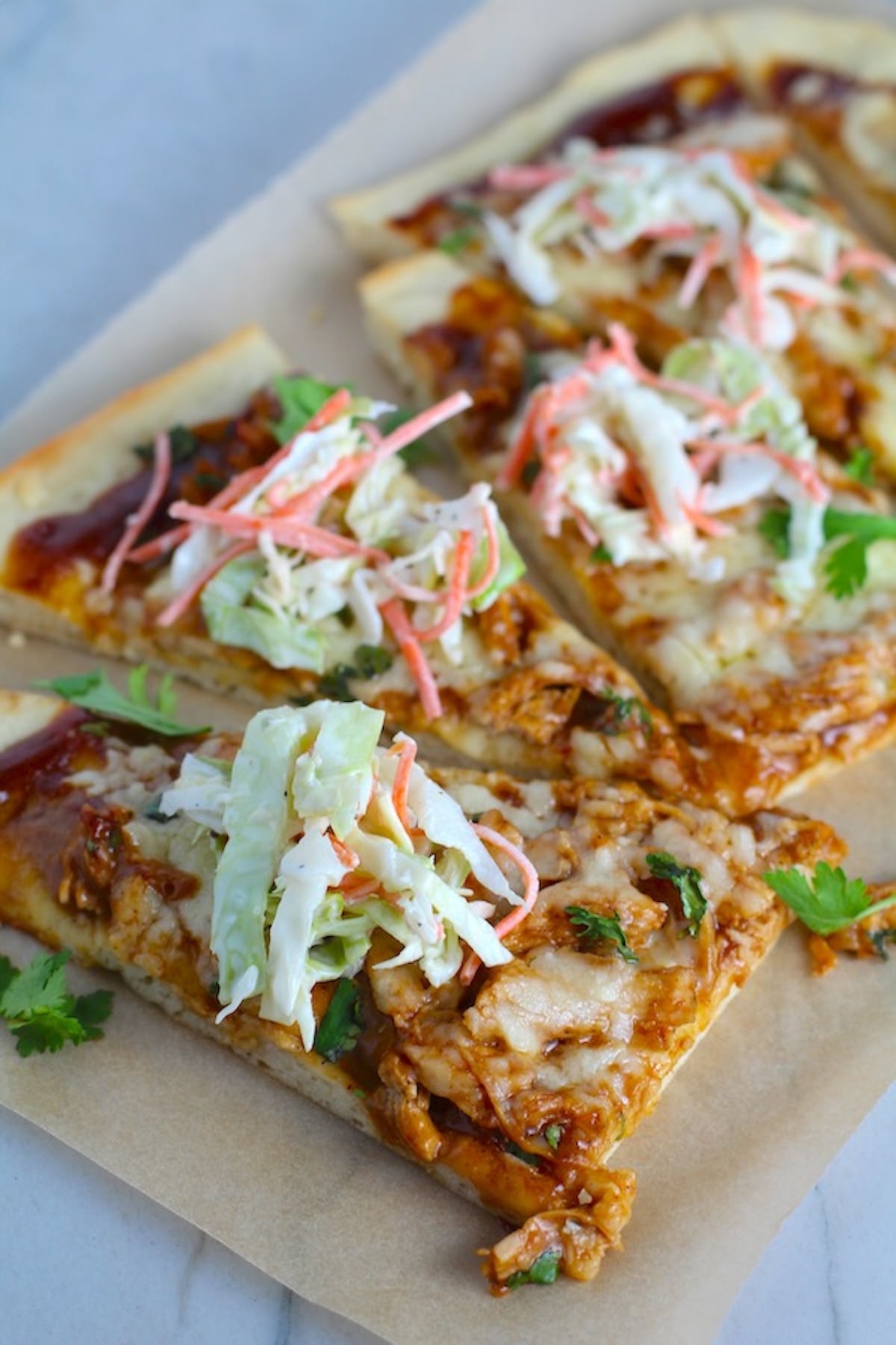 Sliced BBQ Chicken Pizza recipe with coleslaw and cilantro on top. It has homemade pizza crust, tangy and creamy BBQ sauce, hearty shredded chicken, cheddar cheese and coleslaw on top!
