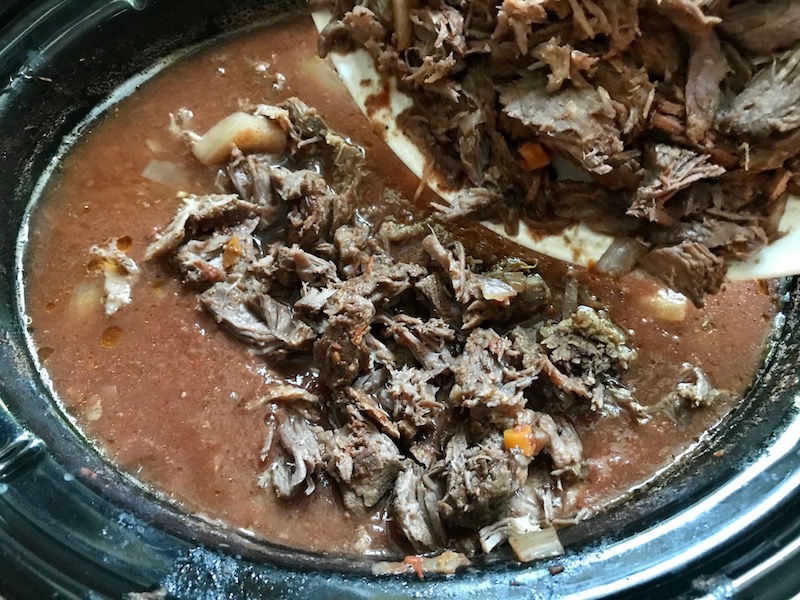 Adding cooked shredded beef to sauce in pot for Shredded Beef Ragu Recipe with Pappardelle. It's so easy to make and has a thick meaty texture and a super rich delicious flavor.
