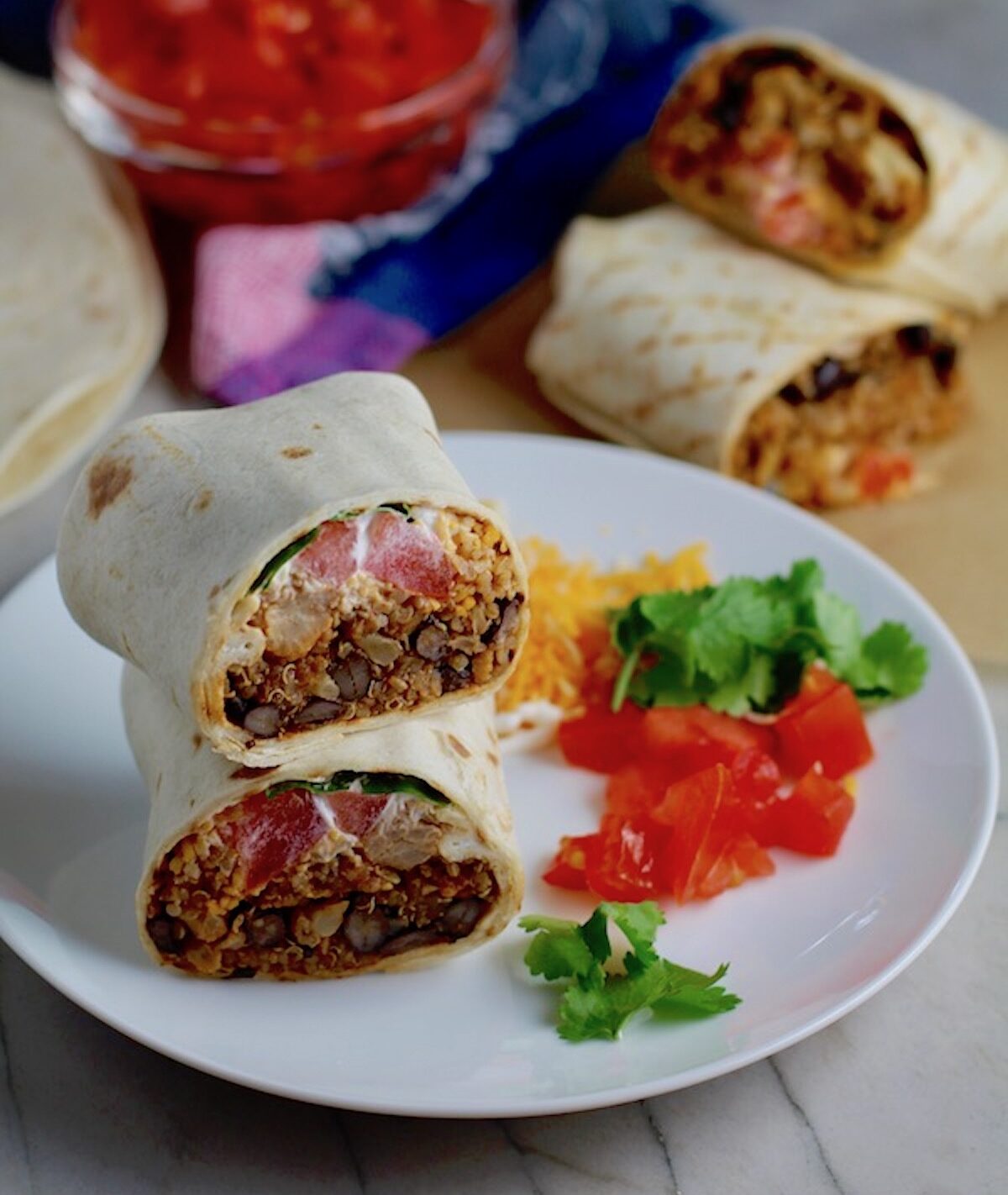 Burritos with Black Beans and Quinoa recipe cut in half and stacked on plate. Packed with protein and fiber, but also cheese, tomato, cilantro, and sour cream!  The vegetarian 'meat' is taco-seasoned quinoa, black beans, and cauliflower.