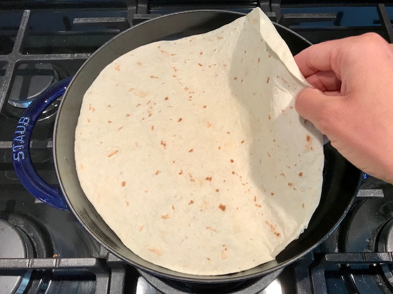 Tortilla in pan for Quinoa Black Bean Burritos. Packed with protein and fiber, but also cheese, tomato, cilantro, and sour cream!  The vegetarian 'meat' is taco-seasoned quinoa, black beans, and cauliflower.
