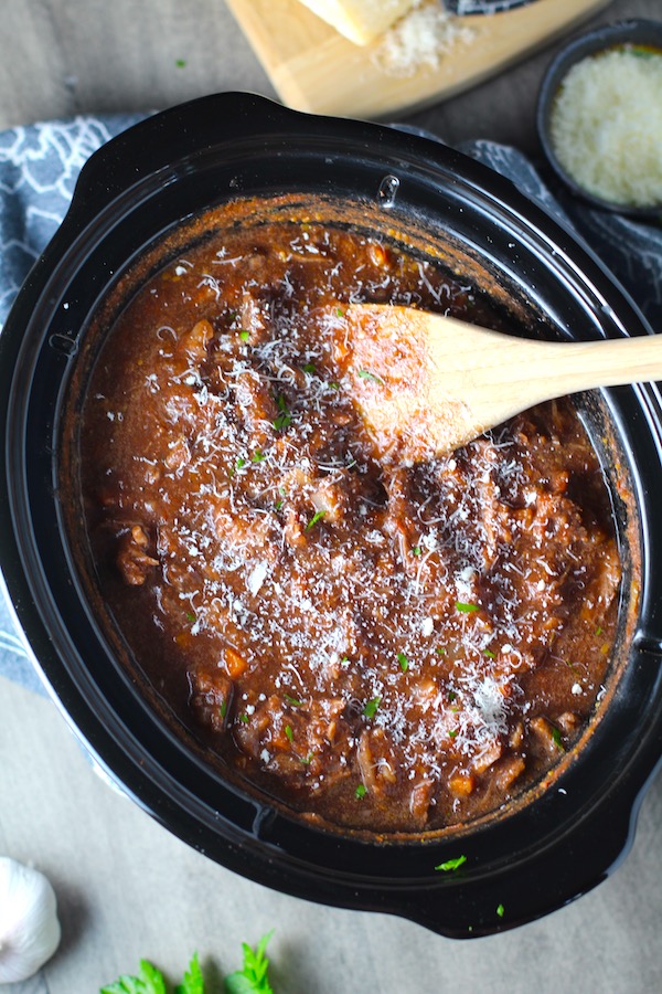 Shredded Beef Ragu Recipe in slow cooker with wood spoon and parmesan on the table. It's so easy to make and has a thick meaty texture and a super rich delicious flavor.