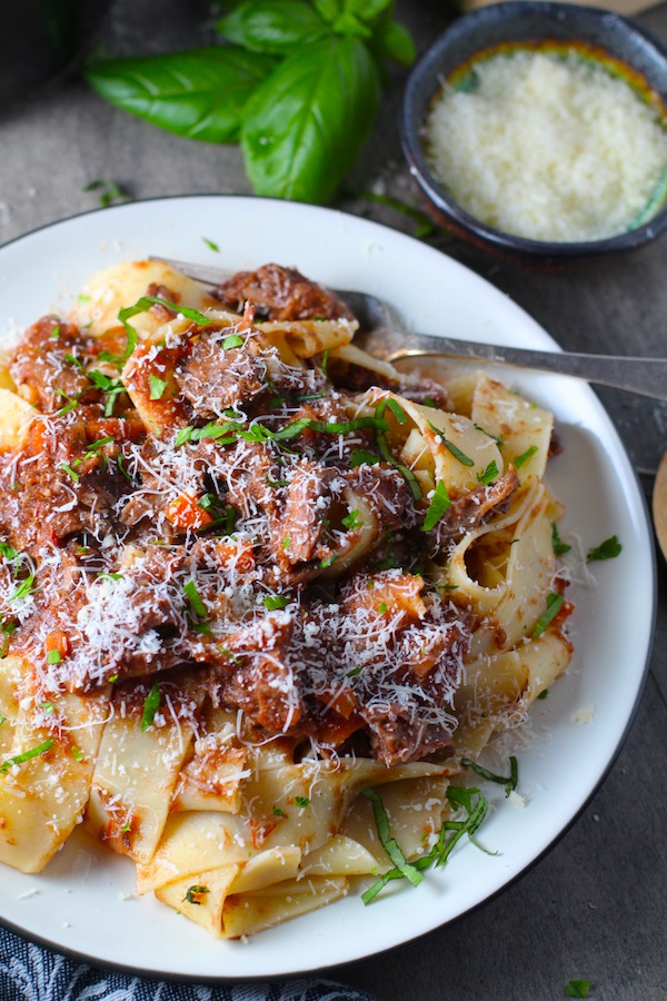 Shredded Beef Ragu Recipe with Pappardelle with a fork on plate with basil and parmesan on the table. It's so easy to make and has a thick meaty texture and a super rich delicious flavor.