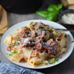 Crockpot Shredded Beef Ragu Recipe with Pappardelle with a fork on plate with parsley, basil, parmesan, and bread on the table. It's so easy to make and has a thick meaty texture and a super rich delicious flavor.