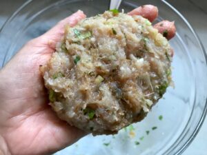 Hand holding a raw chicken patty for a Taco Chicken Burger recipe. The burger has smokey taco seasonings, cilantro, and scallions. Then on top are melty cheese, guacamole, lettuce, tomato, and chipotle mayonnaise!