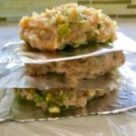 Raw chicken patties stacked between aluminum foil pieces for a Taco Chicken Burger recipe. The burger has smokey taco seasonings, cilantro, and scallions. Then on top are melty cheese, guacamole, lettuce, tomato, and chipotle mayonnaise!
