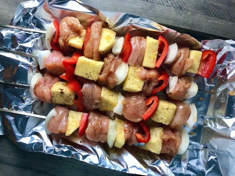 Raw Sweet and Sour Chicken Kabobs with pineapple, onion, and red pepper on aluminum foil covered pan.