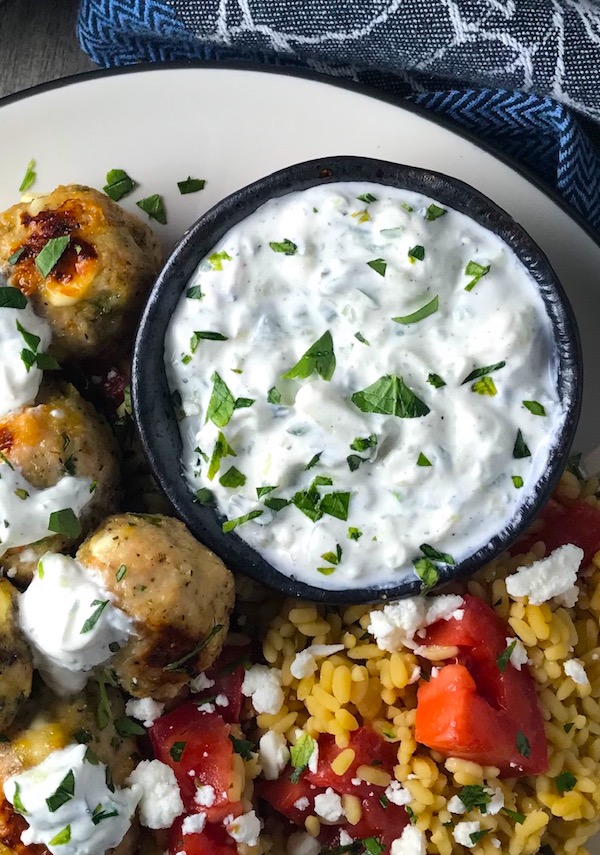 Tzatziki sauce in a bowl on plate with greek meatballs.This is a delicious and easy Tzatziki Recipe with cool and creamy yogurt, fresh cucumber, lime zest, garlic, and scallion.