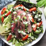 Sliced Grilled Flank Steak Salad Recipe on plate with grilled romaine, halved grape tomatoes, and creamy basil yogurt dressing.
