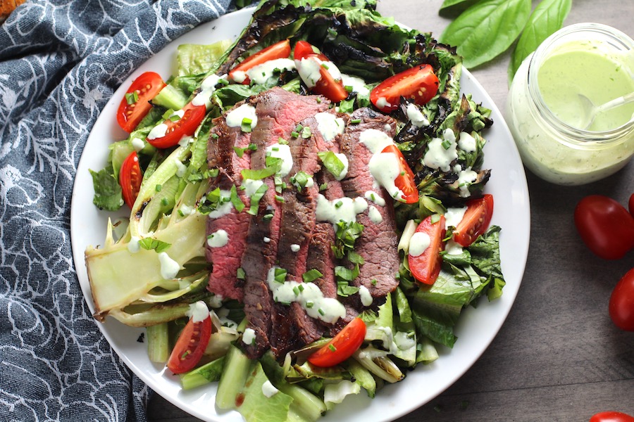 Sliced Grilled Flank Steak Salad Recipe on plate with grilled romaine, halved grape tomatoes, and creamy basil yogurt dressing.