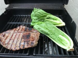 flank steak and romaine lettuce halves on gas grill for Flank Steak Salad Recipe with halved grape tomatoes, and creamy basil yogurt dressing.