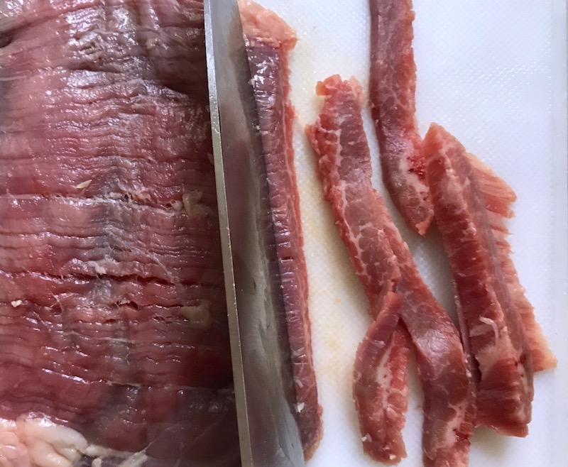 Knife slicing raw flank steak for Korean Beef Tacos with flavorful Korean beef, crunchy Sesame Cabbage Slaw and a creamy, cool, Cilantro Lime Sriracha sauce!