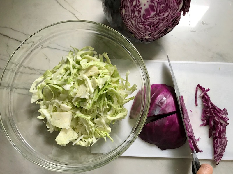 knife slicing purple cabbage with white cabbage in bowl on side for Korean Beef Tacos with flavorful Korean beef, crunchy Sesame Cabbage Slaw and a creamy, cool, Cilantro Lime Sriracha sauce!