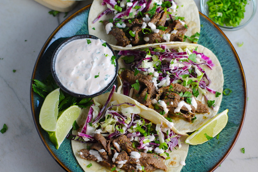 Korean Beef Tacos on a plate with flavorful Korean beef, crunchy Sesame Cabbage Slaw and a creamy, cool, Cilantro Lime Sriracha sauce!