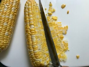 Knife cutting corn off cob for Creamy Corn and Blackened Chicken skillet dinner