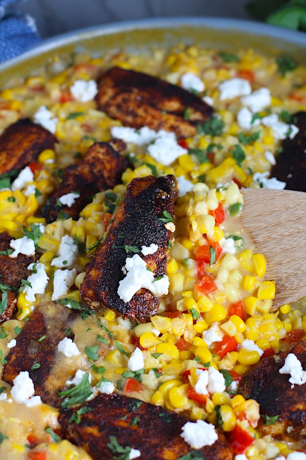 Creamy Corn and Blackened Chicken with feta and cilantro on top in a pan with spatula scooping.
