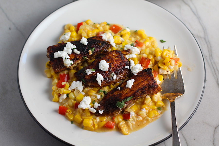 Creamy Corn and Blackened Chicken with feta and cilantro on top on a plate with fork.