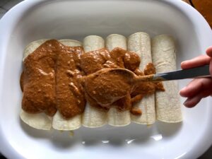 Chicken Mole Enchiladas assembled in dish with spoon scooping mole sauce on top.  The Mole sauce has unsweetened chocolate, tomatoes, green chilis, garlic, adobo sauce, and spices blend harmoniously!