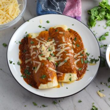 Chicken Enchiladas Mole Sauce Recipe on a plate with cheese and cilantro on top. They are easy to make and delicious! The Mole sauce has unsweetened chocolate, tomatoes, green chilis, garlic, adobo sauce, and spices blend harmoniously!