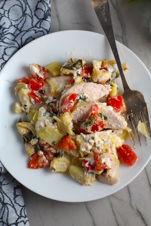 Chicken Artichoke Bake with Tomatoes and Goat Cheese on a plate with fork. It's a creamy, tangy, sweet, savory, mouth watering easy dinner that you can prep ahead!