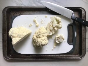 Cauliflower on cutting board in sheet pan with knife for Roasted Garlic Cauliflower Mash.