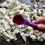 Adding olive oil to chopped cauliflower on sheet pan for Roasted Garlic Cauliflower Mash.