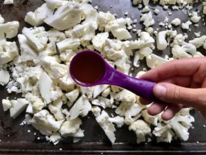 Adding olive oil to chopped cauliflower on sheet pan for Roasted Garlic Cauliflower Mash.