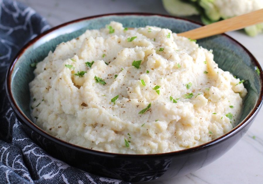 Roasted Garlic Cauliflower Mash in a bowl with spoon. The texture is perfectly creamy and along with the flavor, mimics mashed potatoes.