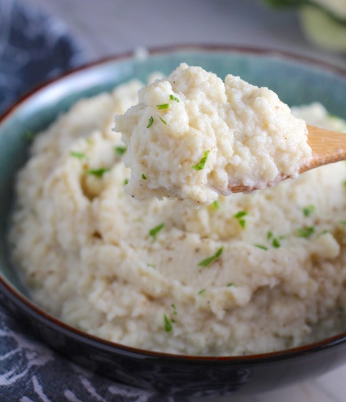 Mashed Roasted Cauliflower in a bowl with spoon scooping. The texture is perfectly creamy and along with the flavor, mimics mashed potatoes.