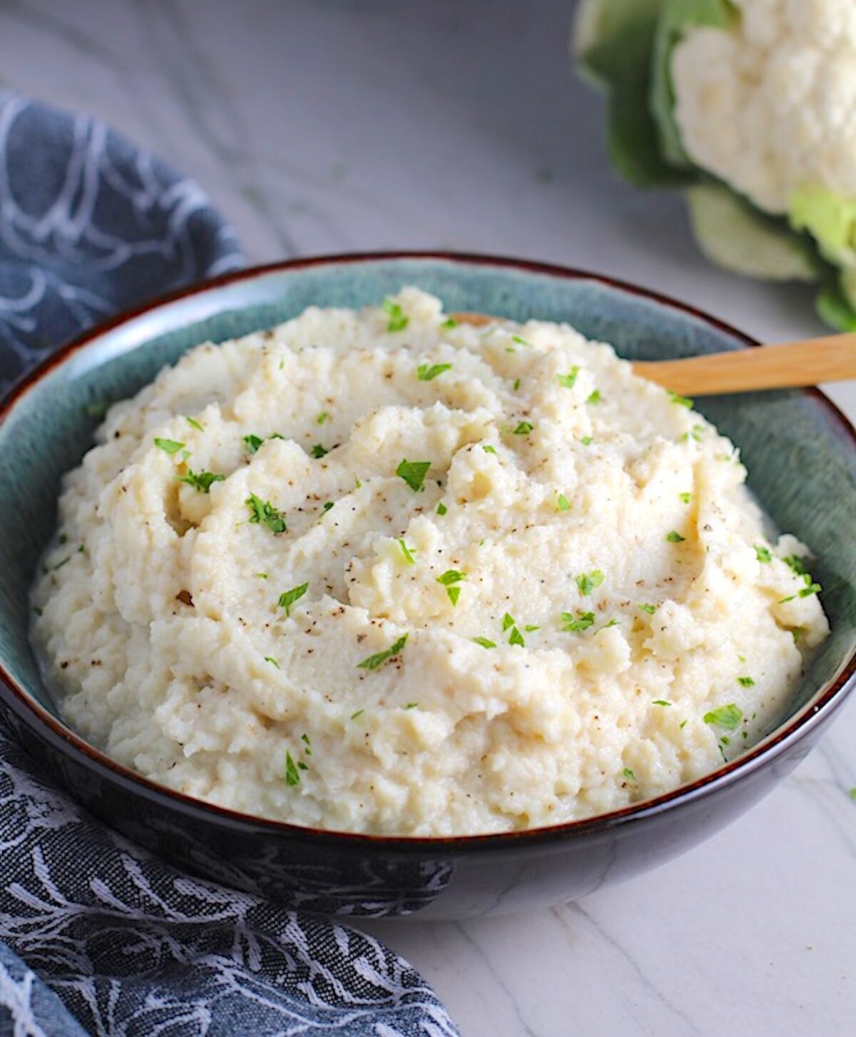 Mashed Roasted Cauliflower in a bowl with spoon. The texture is perfectly creamy and along with the flavor, mimics mashed potatoes.