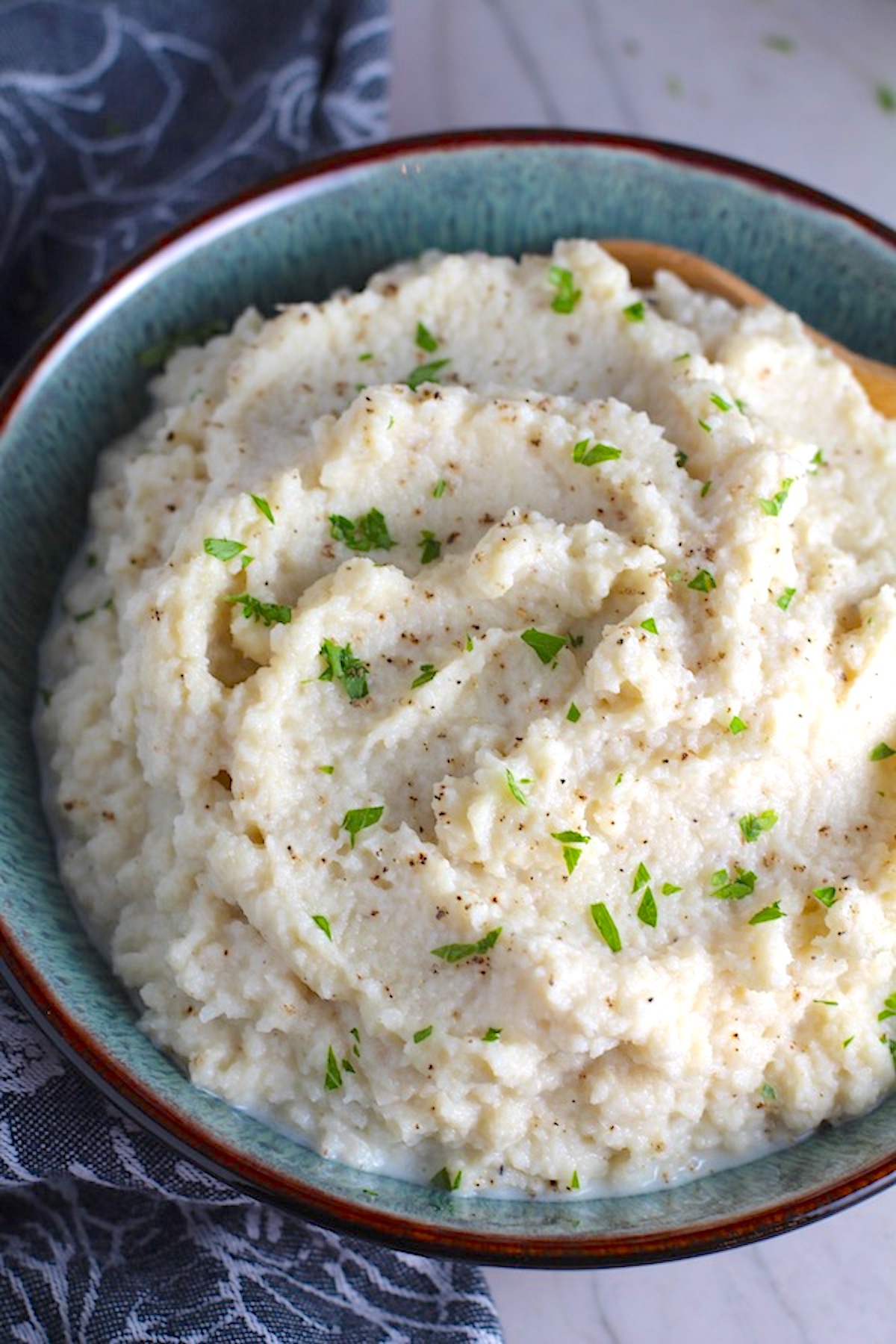 Mashed Roasted Cauliflower in a bowl with spoon. The texture is perfectly creamy and along with the flavor, mimics mashed potatoes.