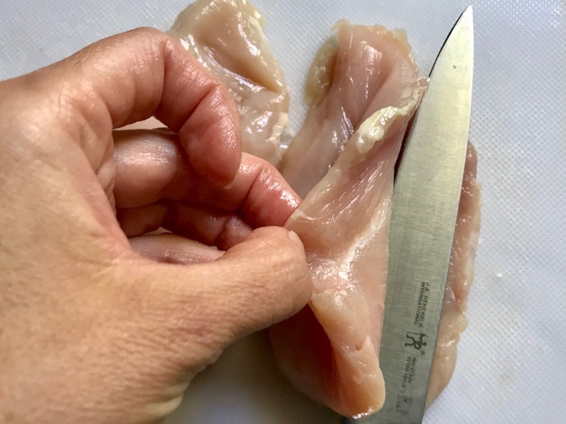 Knife slicing raw chicken for One Pot Chicken Cordon Bleu Bake.  On the bottom you get flavorful rice topped with chicken, salty ham, nutty and melty swiss cheese, and a crunchy breadcrumb topping!