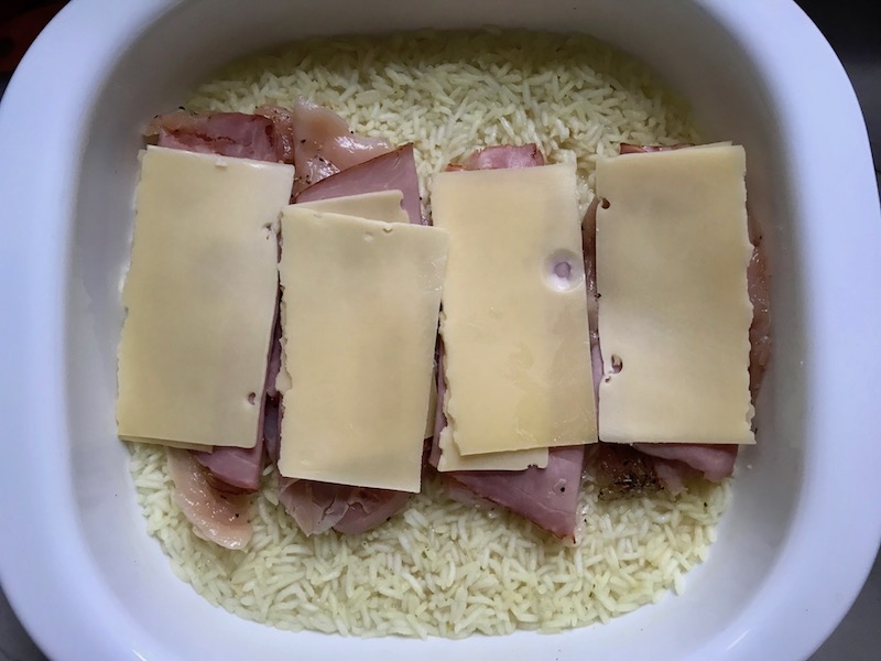 Sliced raw chicken with deli ham and slice of cheese on top for One Pot Chicken Cordon Bleu Bake.  On the bottom you get flavorful rice topped with chicken, salty ham, nutty and melty swiss cheese, and a crunchy breadcrumb topping!