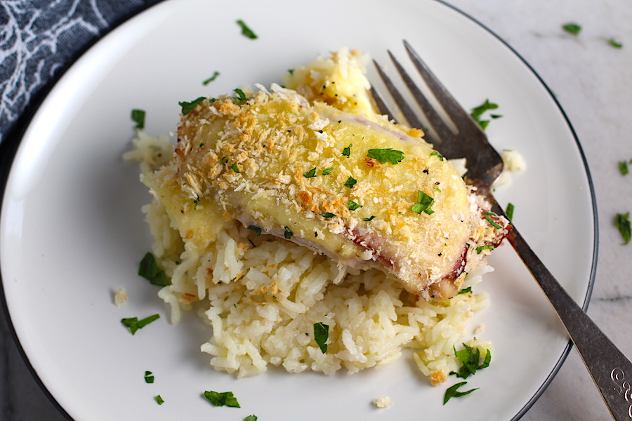 Piece of One Pot Chicken Cordon Bleu Bake on a plate with fork.  On the bottom you get flavorful rice topped with chicken, salty ham, nutty and melty swiss cheese, and a crunchy breadcrumb topping!