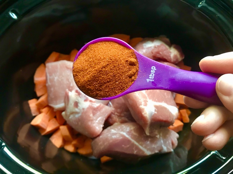 Adding paprika to raw pork and veggies in slow cooker insert for Paprika Pork Stew Recipe with carrots, onion, parsley.