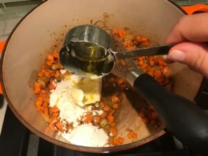 Flour being added to carrots and onions in pot for Creamy Chicken Sausage and Tortellini Soup. It's silky and creamy with onions, garlic, Chicken sausage, and zucchini bring so much flavor and texture.  The tortellini give that delicious salty, creamy, hearty bite! 