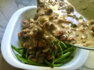 Chorizo and mushroom sauce being poured over green beans in casserole dish for Creamy Green Beans and Mushrooms with Chorizo in a serving bowl are a creamy and savory side dish.