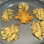 Lentil and Zucchini Cakes starting to cook in a frying pan with center cake flipped over. They have a crispy outside and soft inside and are perfect for an easy dinner!  The flavors are simple but perfect with parmesan, oregano, scallions, lentils, and zucchini.