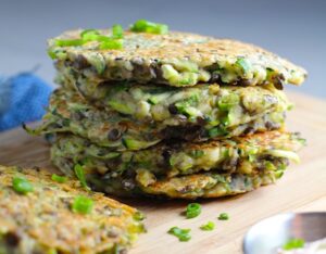 Lentil and Zucchini Cakes stacked on wood cutting board. They have a crispy outside and soft inside and are perfect for an easy dinner!  The flavors are simple but perfect with parmesan, oregano, scallions, lentils, and zucchini.