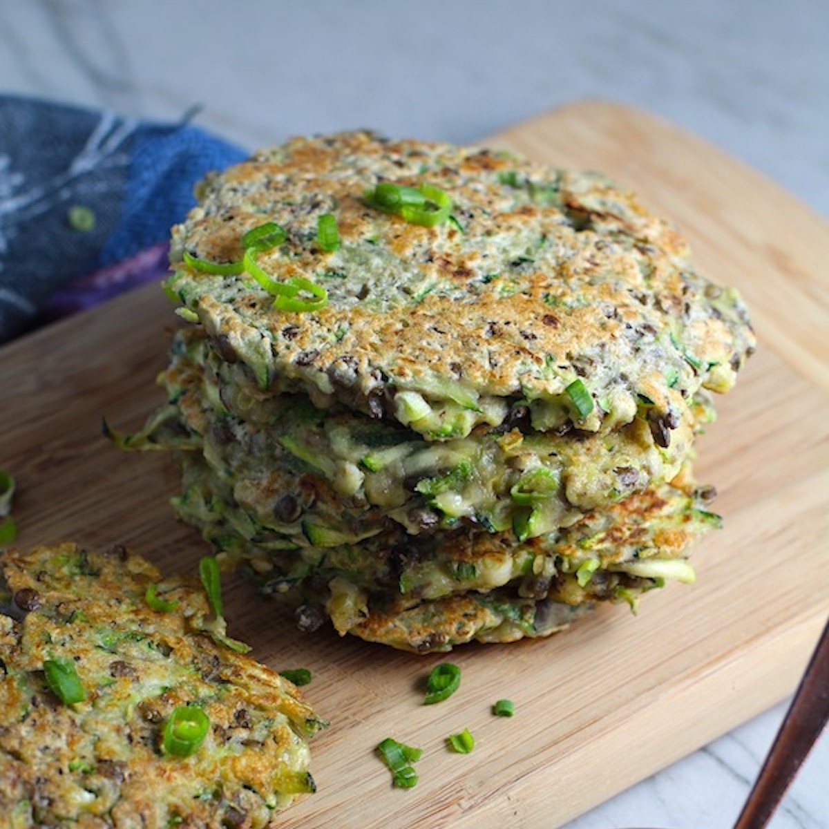 Zucchini Lentil Fritters stacked on wood cutting board. They have a crispy outside and soft inside and are perfect for an easy dinner!  The flavors are simple but perfect with parmesan, oregano, scallions, lentils, and zucchini.