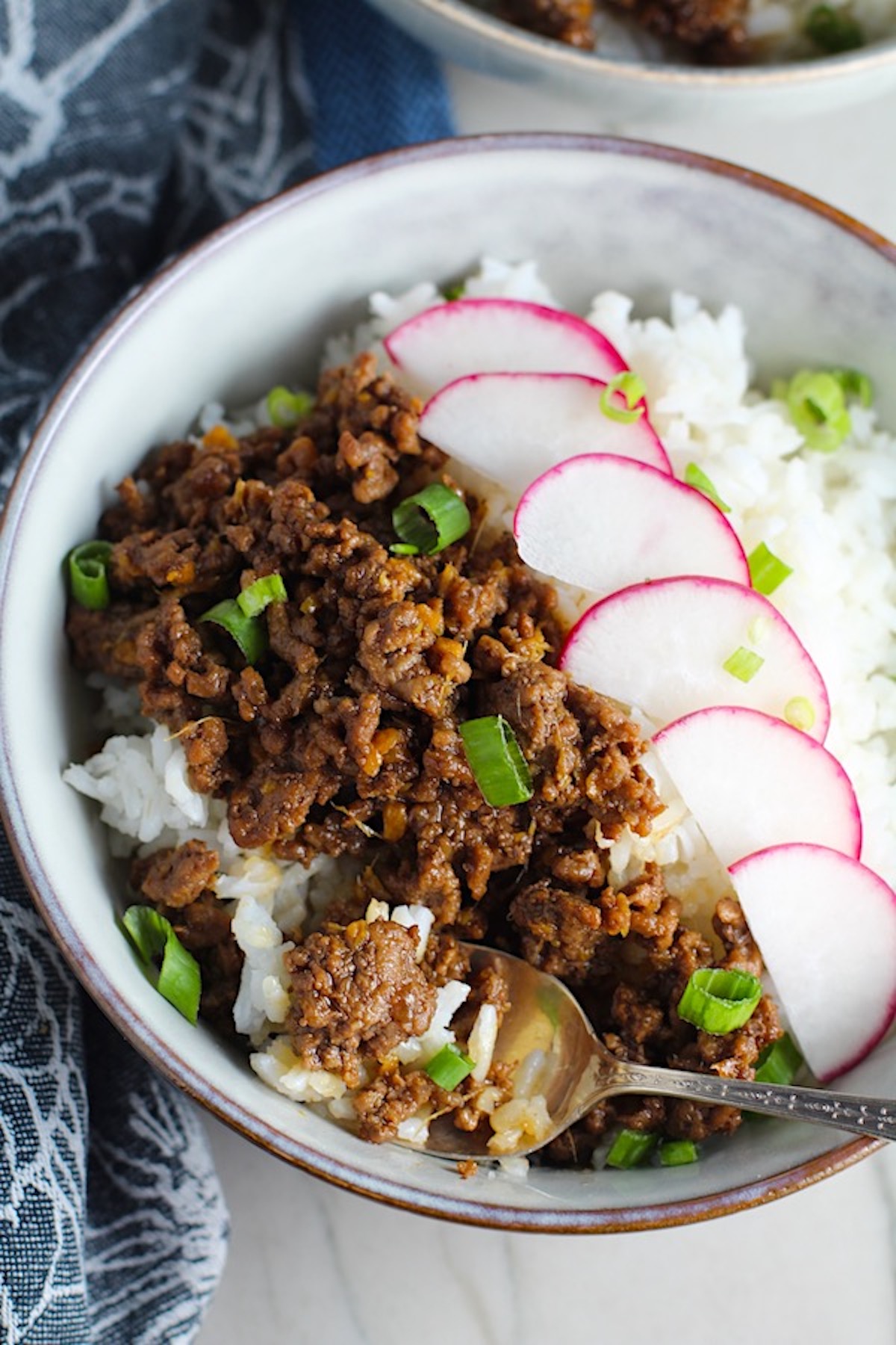 Korean Bulgogi Ground Beef and Rice Bowl with sliced radishes fanned out on top and scallion garnish.