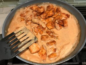 Spatula mixing cooked chicken into sauce in a frying pan for Quick Cooking Creamy Chicken Paprika. It's creamy, smokey, rich, and hearty. This is an easy weeknight family dinner!