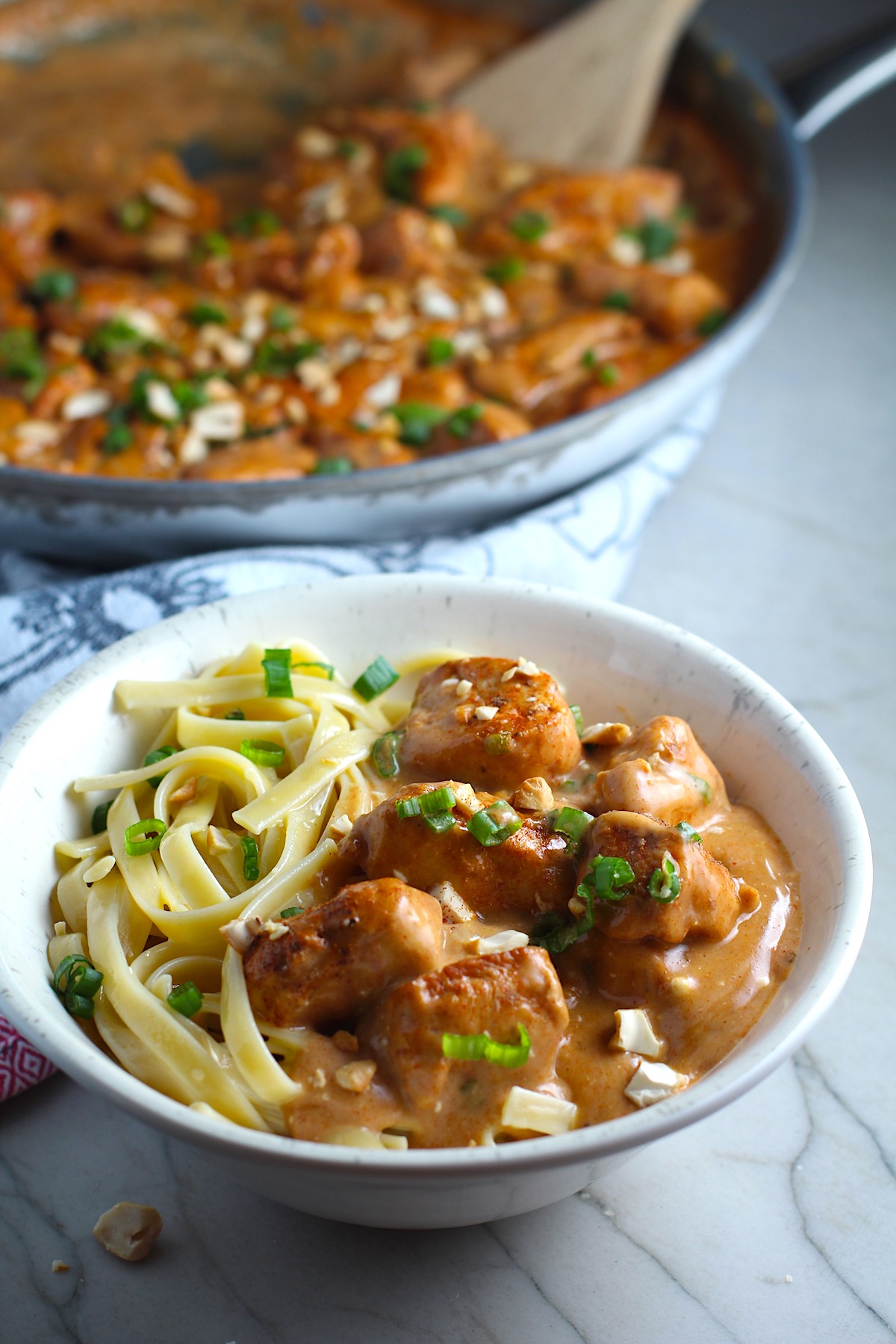 Quick Cooking Creamy Chicken Paprika in a bowl with pasta and pan in background. It's creamy, smokey, rich, and hearty. This is an easy weeknight family dinner!