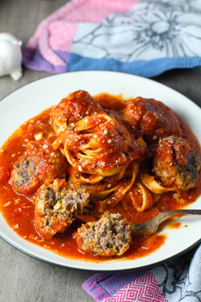 Healthy Meatballs with Zucchini & Lean Beef on a plate with tomato sauce and fettuccine in the center. They're loaded with flavor from the garlic, minced onion, salt, and pepper.  The zucchini brings moisture, texture, and bulks up the meatballs with healthiness.