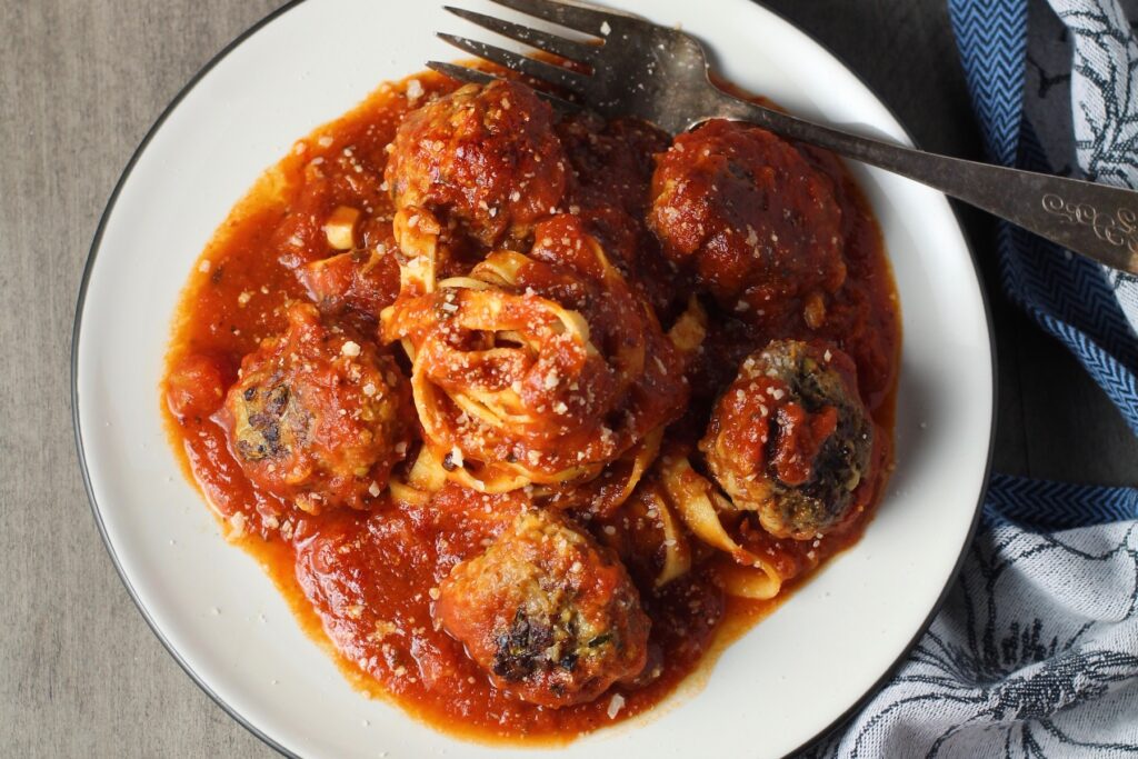Healthy Meatballs with Zucchini & Lean Beef on a plate with tomato sauce and fettuccine in the center. They're loaded with flavor from the garlic, minced onion, salt, and pepper. The zucchini brings moisture, texture, and bulks up the meatballs with healthiness.