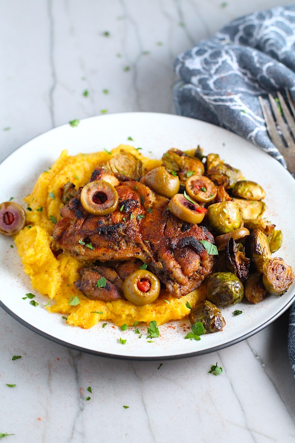 Sheet Pan Spanish Chicken thighs on a plate with Butternut Squash Mash, Olives, and Brussels Sprouts!  It's warm, hearty, and smoky.