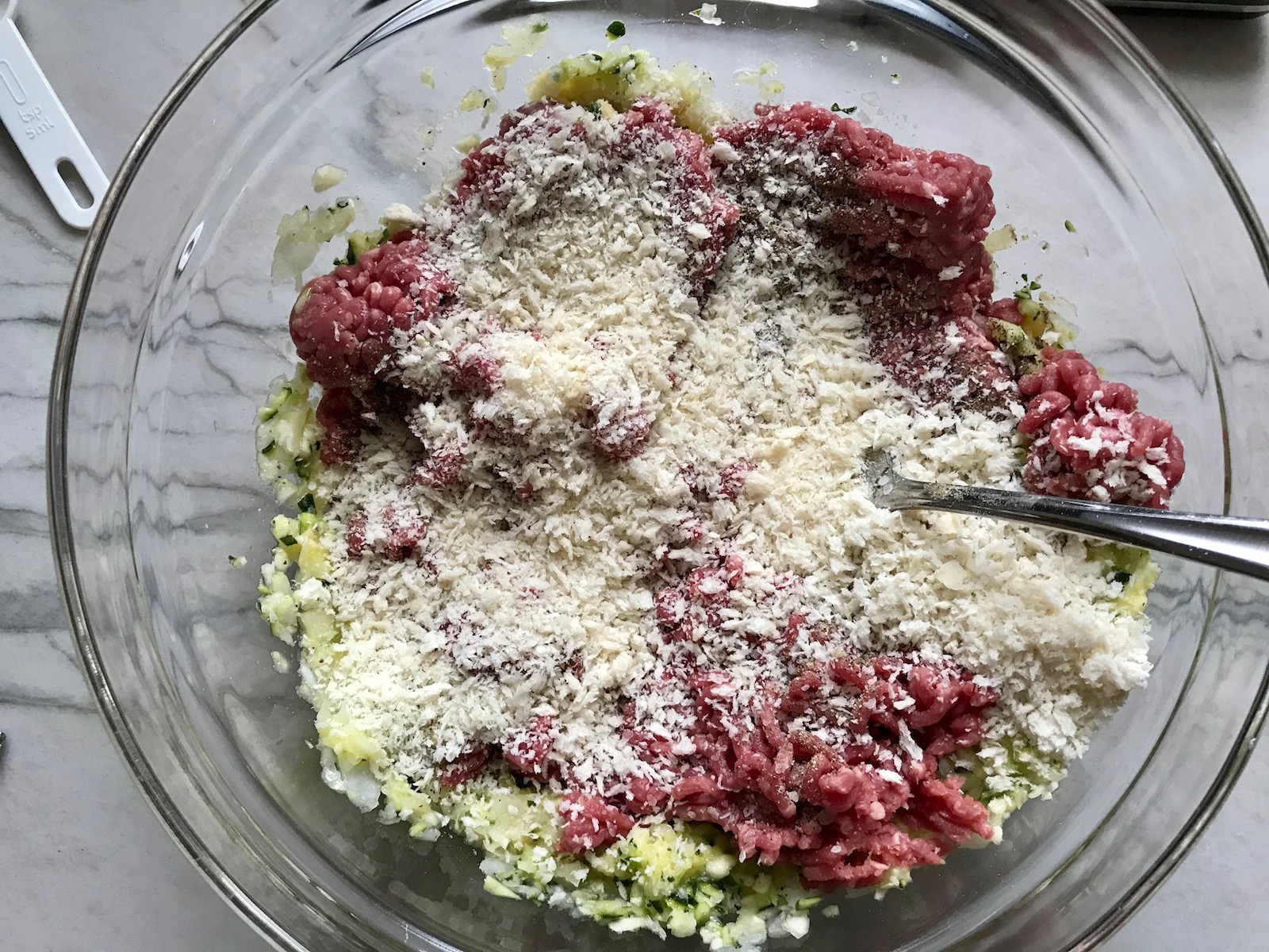 Ingredients in bowl for Healthy Meatballs with Zucchini & Lean Beef. They're loaded with flavor from the garlic, minced onion, salt, and pepper. The zucchini brings moisture, texture, and bulks up the meatballs with healthiness.