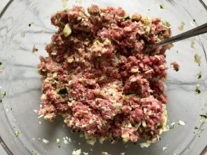 Meatball ingredients mixed in bowl for Healthy Meatballs with Zucchini & Lean Beef. They're loaded with flavor from the garlic, minced onion, salt, and pepper.  The zucchini brings moisture, texture, and bulks up the meatballs with healthiness.