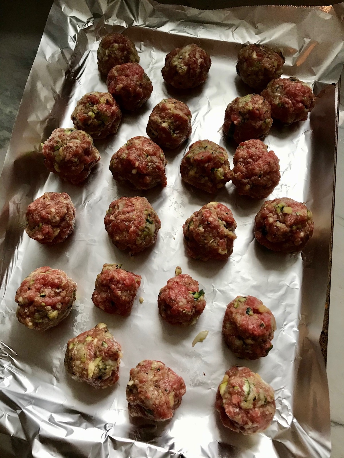 Raw meatballs on pan for Healthy Meatballs with Zucchini & Lean Beef. They're loaded with flavor from the garlic, minced onion, salt, and pepper. The zucchini brings moisture, texture, and bulks up the meatballs with healthiness.